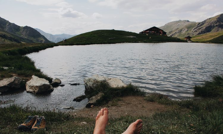 barefooted person lying on grass viewing lake and mountain