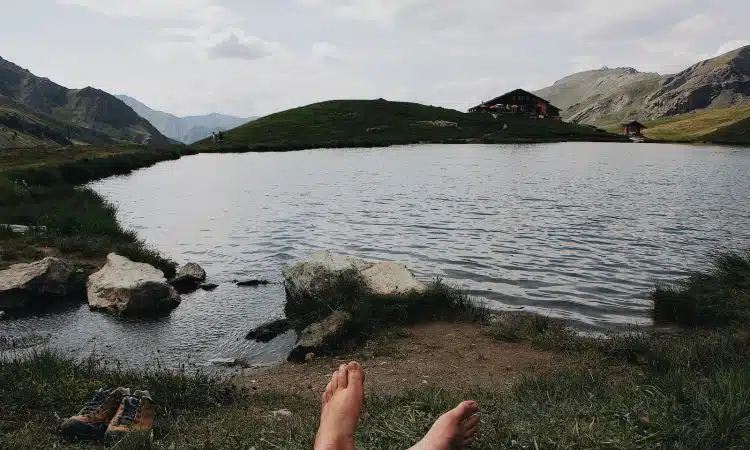 barefooted person lying on grass viewing lake and mountain