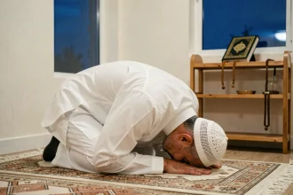 Homme en prière de l'aube en position de sujud sur un tapis de prière à motifs géométriques dans un coin de prière domestique